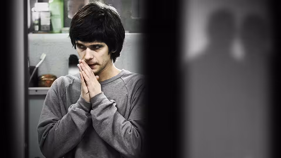 Ben Coulter (Ben Whishaw) stands indoors with his hands clasped beneath his chin