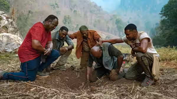 Four men gather around Paul as he kneels in disturbed earth in the jungle