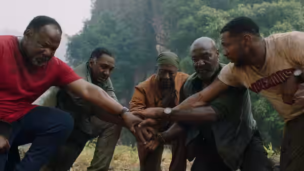 Five men stack their hands together in a forest clearing