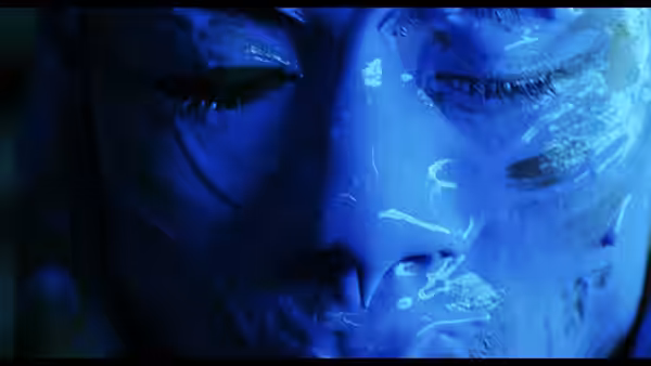 A close-up face with closed eyes reflects blue light