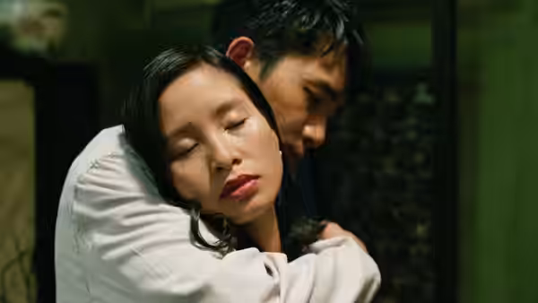 A man embraces a woman from behind in a dim room