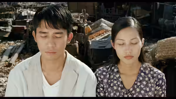 A man and woman sit with closed eyes among crowded rooftop shacks