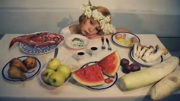 A flower-crowned woman leans over a table covered with fruit and plates