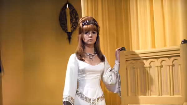 Francesca (Jane Asher) stands beside a carved cabinet in a white gown