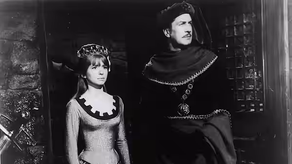A woman in a crown stands beside a masked man in a dark costume