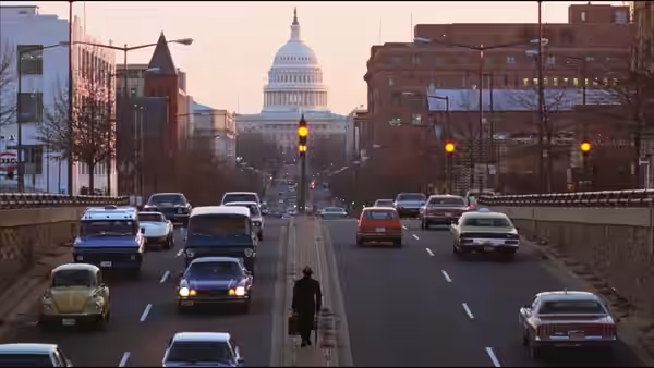 a pedestrian crossing a busy multi-lane road with traffic and the Capitol behind