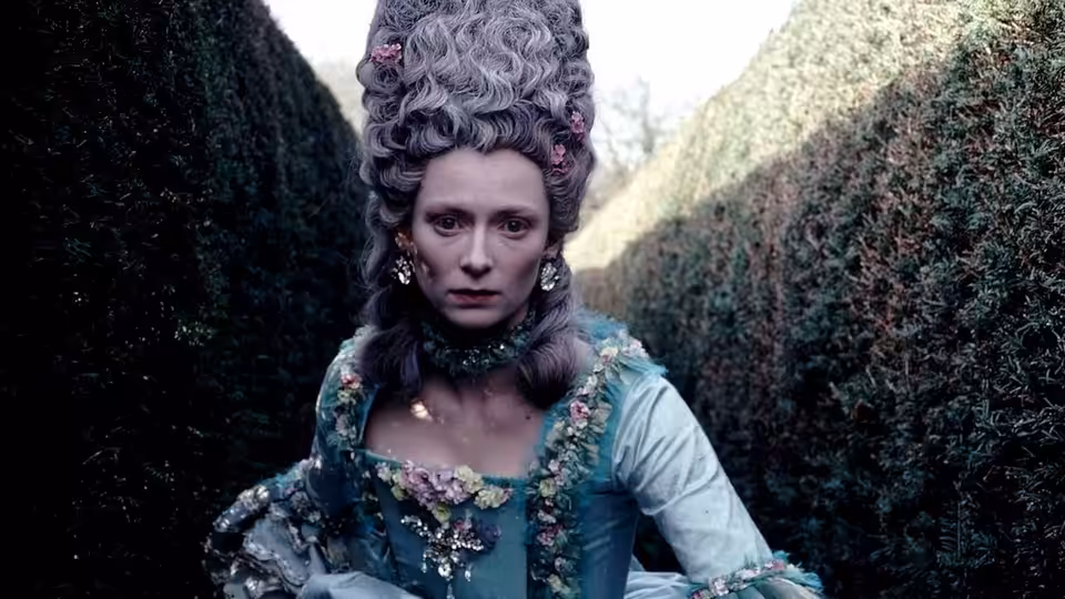 Tilda Swinton as Orlando in an ornate blue gown between tall hedges