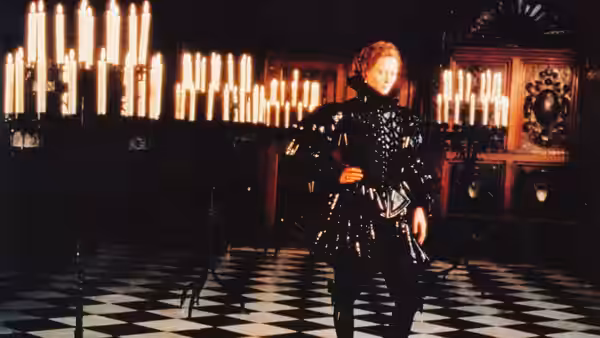 Tilda Swinton as Orlando posing in a black costume in a candlelit hall