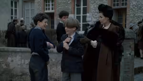 A woman in a fur coat talks with two boys outside a building
