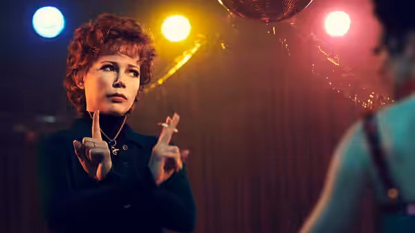 Gwen Verdon (Michelle Williams) gestures with raised hands in a nightclub with colorful lights