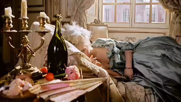 A woman and man lie together in bed behind a table of candles and wine