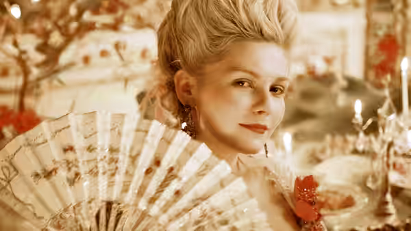 Marie Antoinette (Kirsten Dunst) holds a fan beside a candlelit table