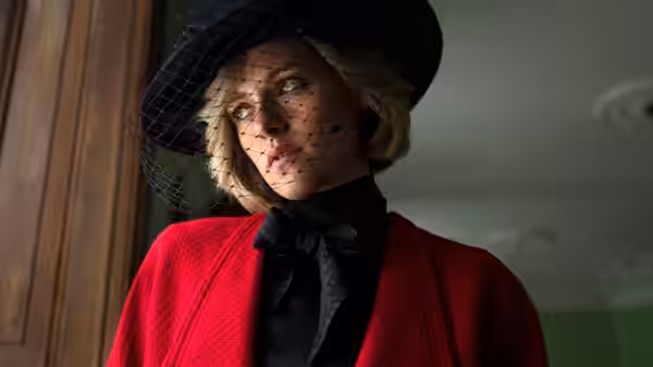 Diana (Kristen Stewart) wears a red coat and veiled black hat by a window