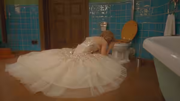 Diana (Kristen Stewart) in a wedding gown leans over a toilet in a tiled bathroom