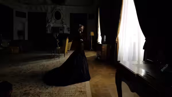 Diana (Kristen Stewart) stands in a long black gown beside a bright window