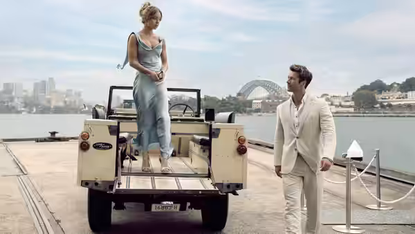 Bea (Sydney Sweeney) standing on a vintage vehicle as Ben (Glen Powell) looks on by the harbor