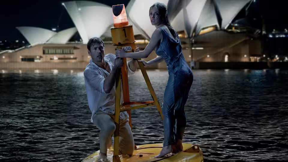 Bea (Sydney Sweeney) and Ben (Glen Powell) on a raft holding a light near the Opera House at night