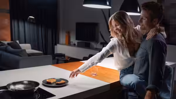 Bea (Sydney Sweeney) reaching across the counter as Ben (Glen Powell) sits beside her in the kitchen