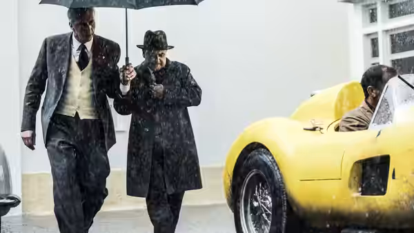 two men walking under an umbrella beside a yellow racing car in the rain