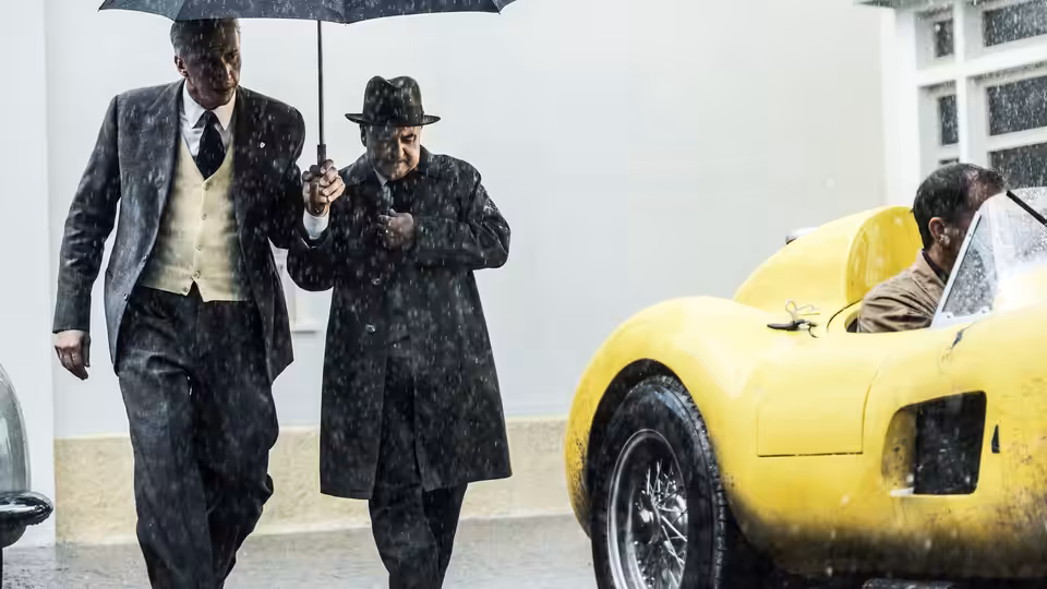 two men walking under an umbrella beside a yellow racing car in the rain