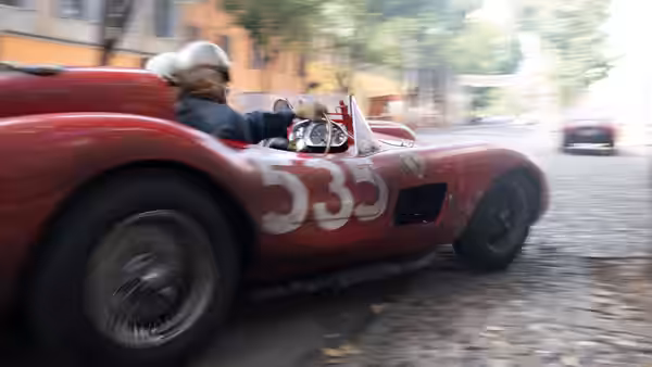 driver in helmet steering a red racing car on a cobblestone street