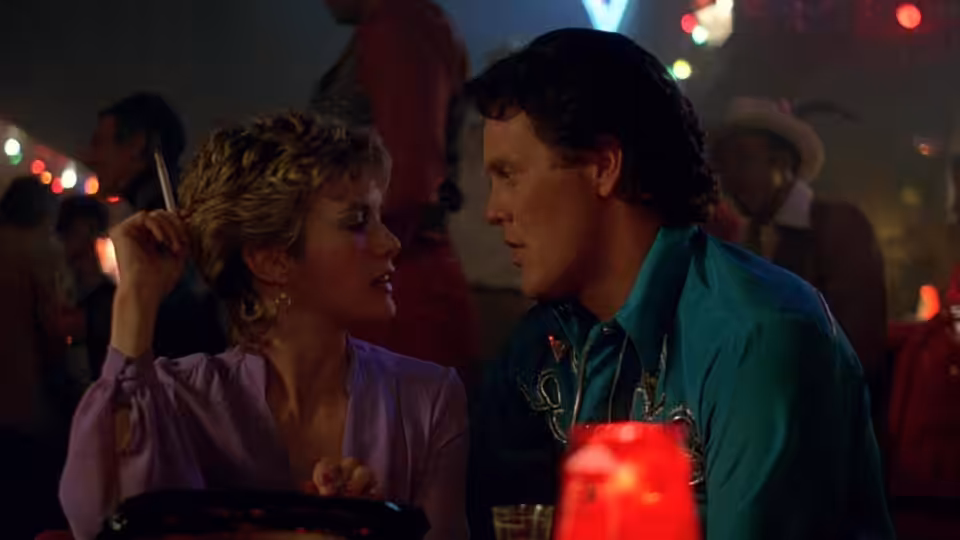 Princess (Season Hubley) talks with Ramrod (Wings Hauser) at a crowded nightclub table