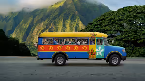 A colorful bus driving along a road with green mountains behind
