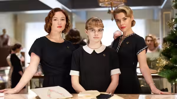 Lisa (Angourie Rice) stands between two women in black at a department-store counter