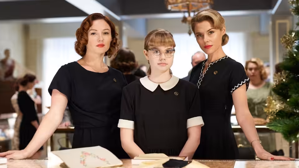 Lisa (Angourie Rice) stands between two women in black at a department-store counter