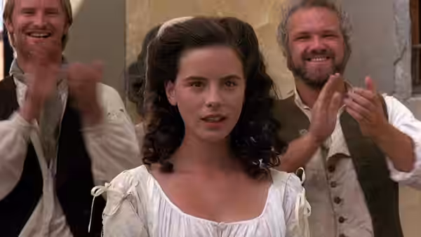 Hero (Kate Beckinsale) standing between two clapping men in a hall