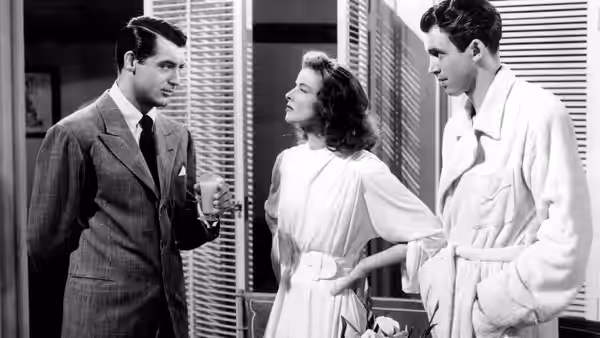 C.K. Dexter Haven (Cary Grant) with drink faces Tracy Lord (Katharine Hepburn) and Mike Connor (James Stewart)