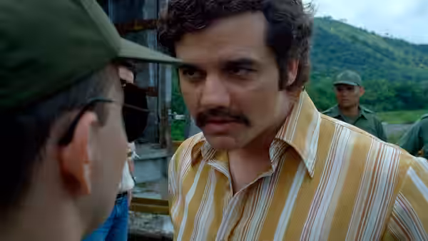 Pablo Escobar (Wagner Moura) in a striped shirt facing another man outdoors