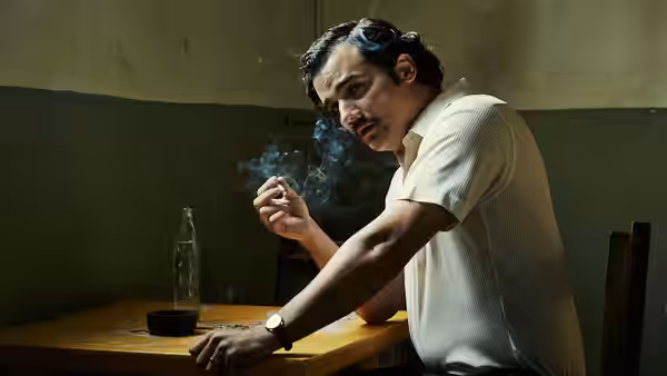 Pablo Escobar (Wagner Moura) smoking a cigarette at a wooden table