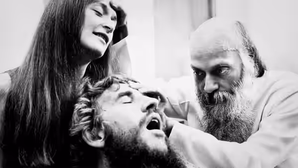 Bhagwan Shree Rajneesh touches the forehead of a bearded man with closed eyes
