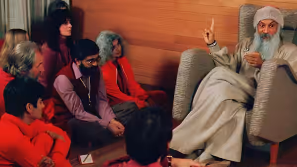 Bhagwan Shree Rajneesh points upward while seated among followers in red attire