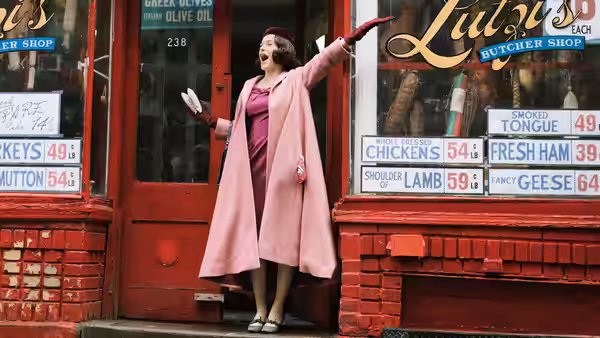 Midge Maisel (Rachel Brosnahan) gesturing outside a butcher shop storefront