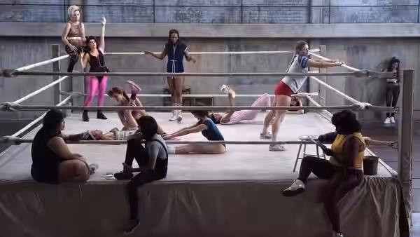 Group of female wrestlers stand and rest together inside a large ring