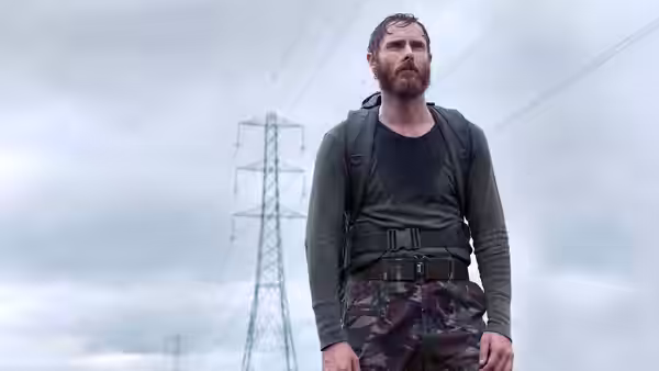 Bearded man with backpack stands under power lines in camouflage trousers