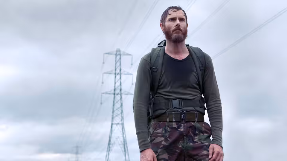 Bearded man with backpack stands under power lines in camouflage trousers