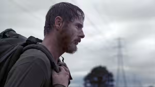 Bearded man with wet hair looks aside while holding backpack strap