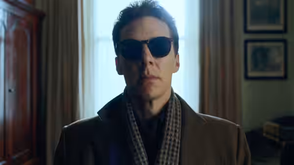 Patrick Melrose (Benedict Cumberbatch) wearing sunglasses and a brown coat indoors