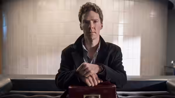 Patrick Melrose (Benedict Cumberbatch) clasping hands on a red case indoors