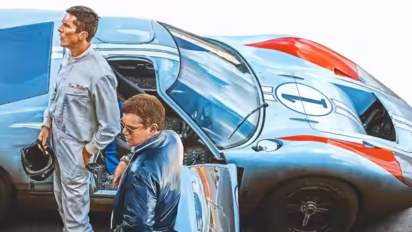 Ken Miles (Christian Bale) leaning into a blue race car beside Carroll Shelby (Matt Damon)