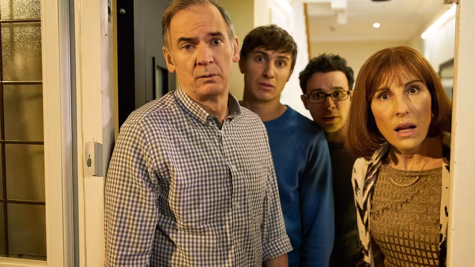 Martin Goodman (Paul Ritter) and Jackie Goodman (Tamsin Greig) stand surprised in a doorway with two young men behind