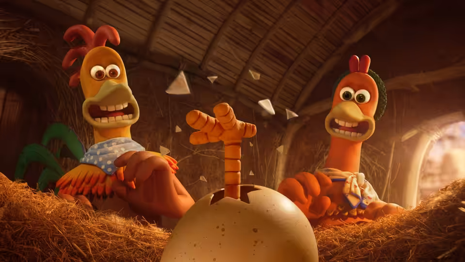 Two chickens sit beside a cracked egg in a straw-filled coop