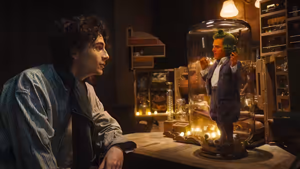Timothée Chalamet watching Hugh Grant as an Oompa Loompa in a glass case