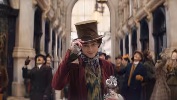 Willy Wonka (Timothée Chalamet) tipping his hat on a crowded city street