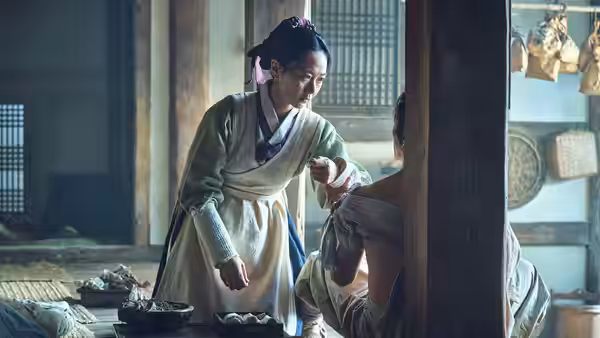 Woman in traditional robe tends to the back of a seated injured man