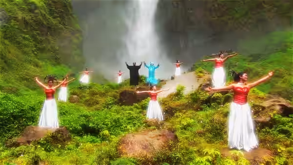 Women in red and white costumes raise their arms in dance formation before a waterfall