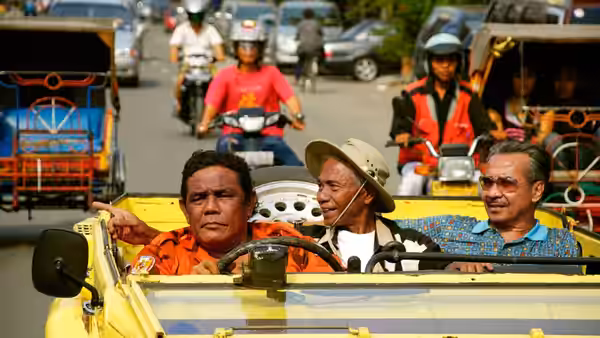 Three men ride in a yellow open car through busy urban traffic on a city street